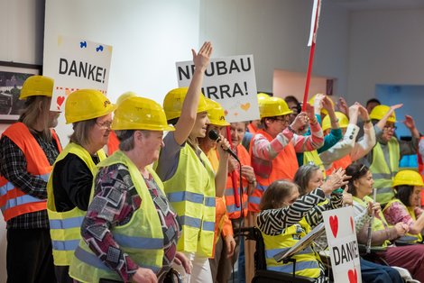 Mehrere mit Warnwesten und Schildern und Rollstühlen ausgestattete Menschen stehen neben- und hintereinander.